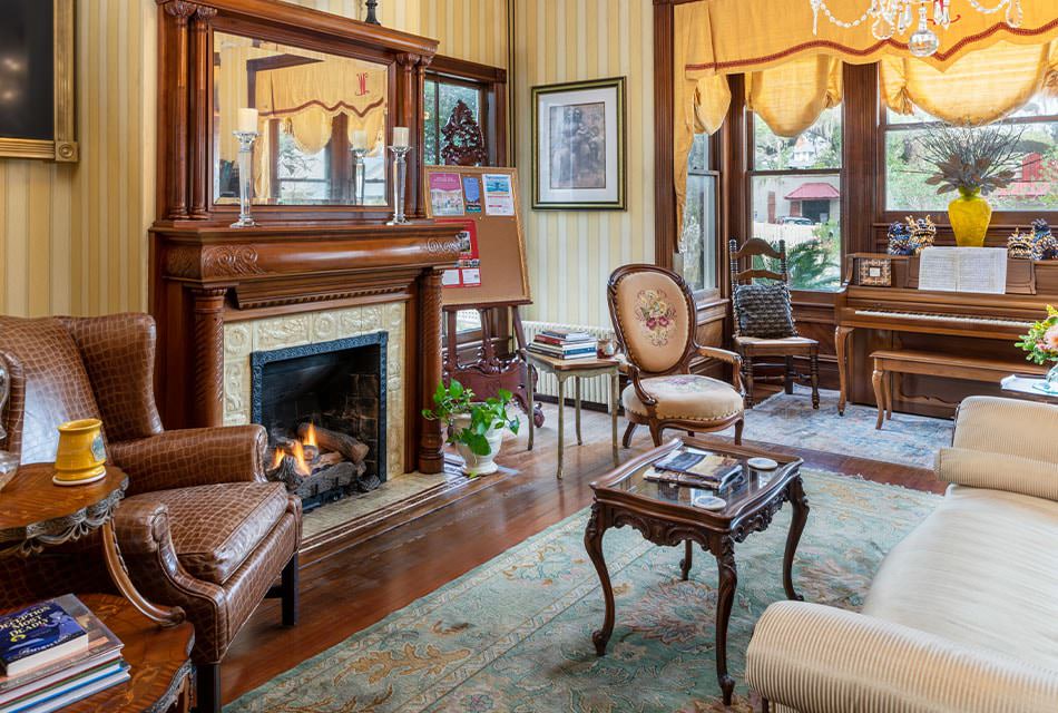 Large room with pale yellow striped wallpaper, hardwood flooring, wooden fireplace, upholstered sofa, and small piano