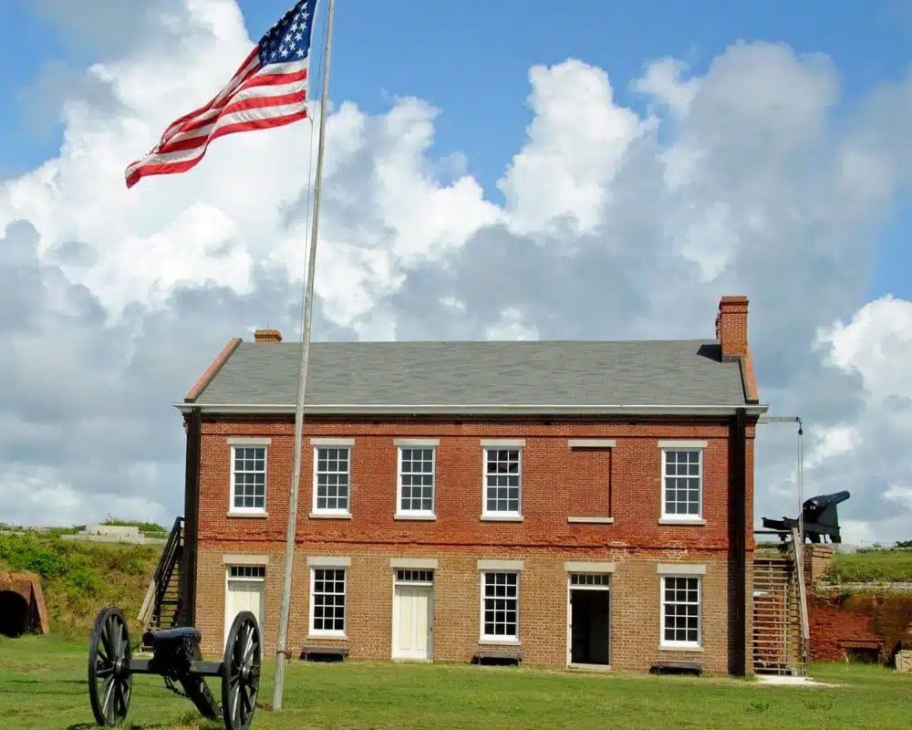 Fort Clinch brick commissary building with American flag flying out front and cannons in the background with green grass and cloudy blue sky