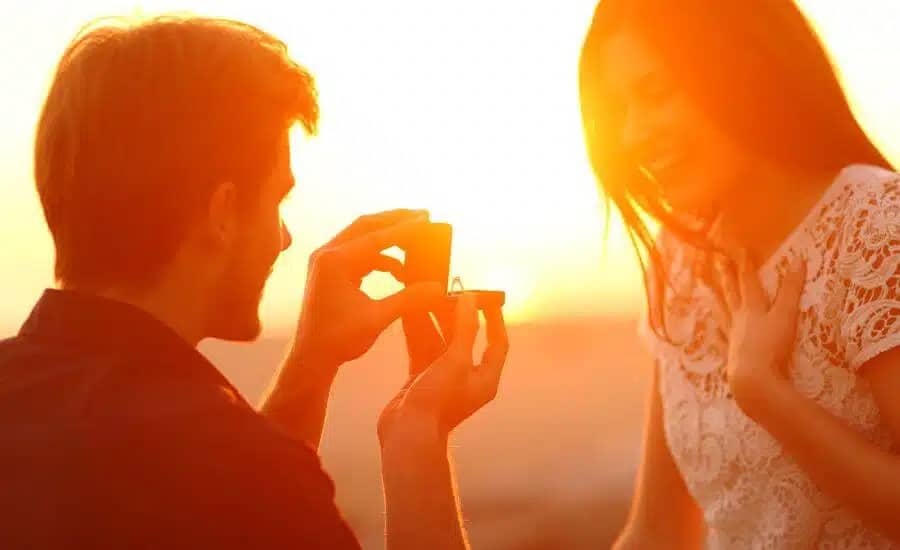 man holding a ring proposing to a woman on the beach at sunset