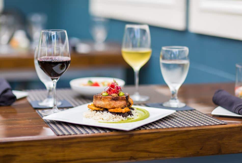 Close up view of food on a square plate and red wine in a glass