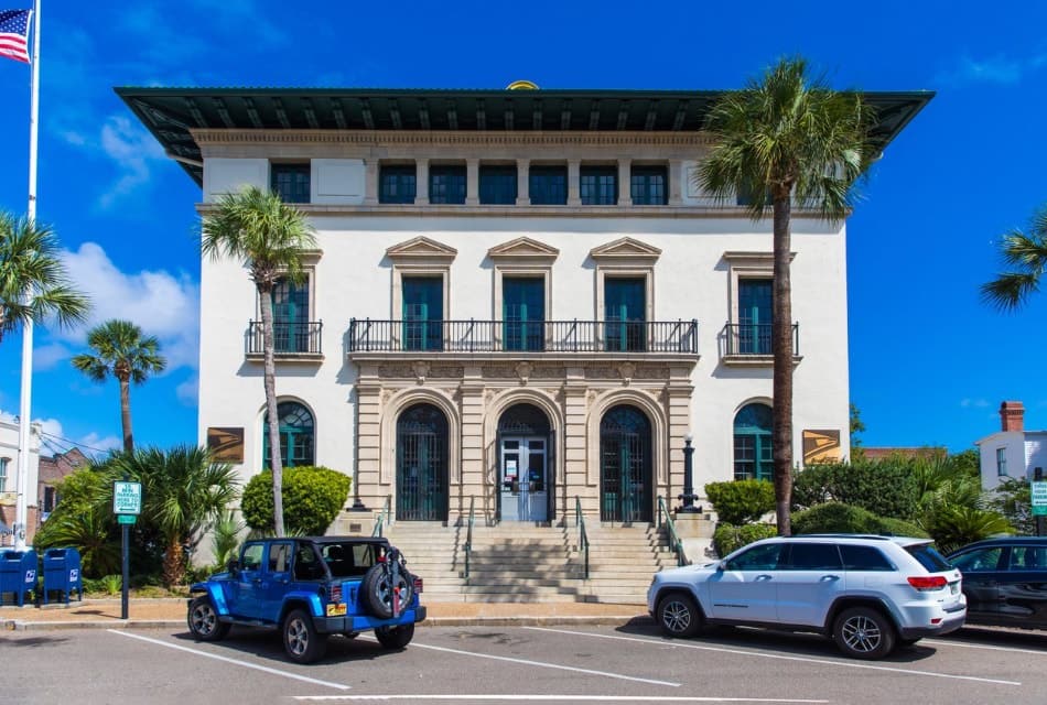 Exterior view of a historic building surrounded by palm trees and green bushes in down town area