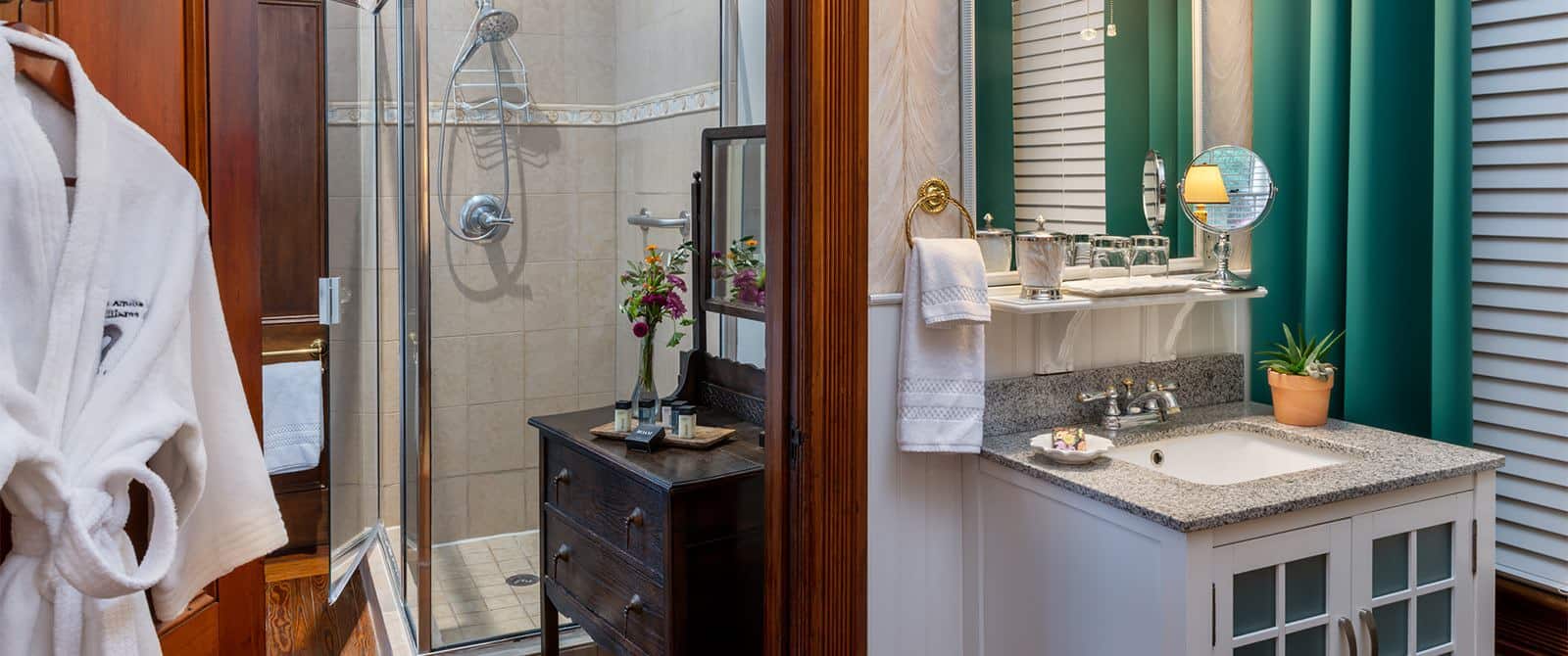 Bathroom with wallpaper and white paneling, tiled stand up shower, white vanity, and wooden dresser