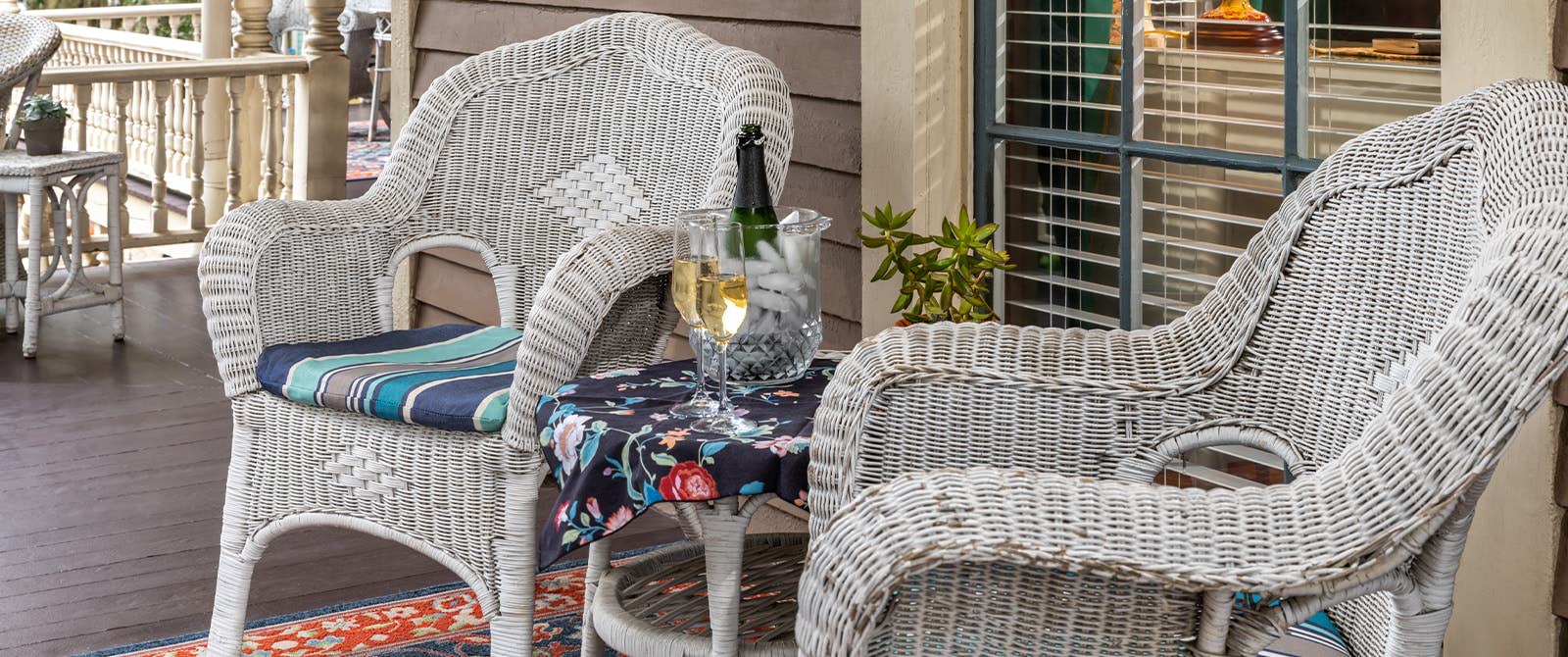 Close up view of white wicker patio chairs and table with glasses filled with Champagne and bottle chilling in vase with ice