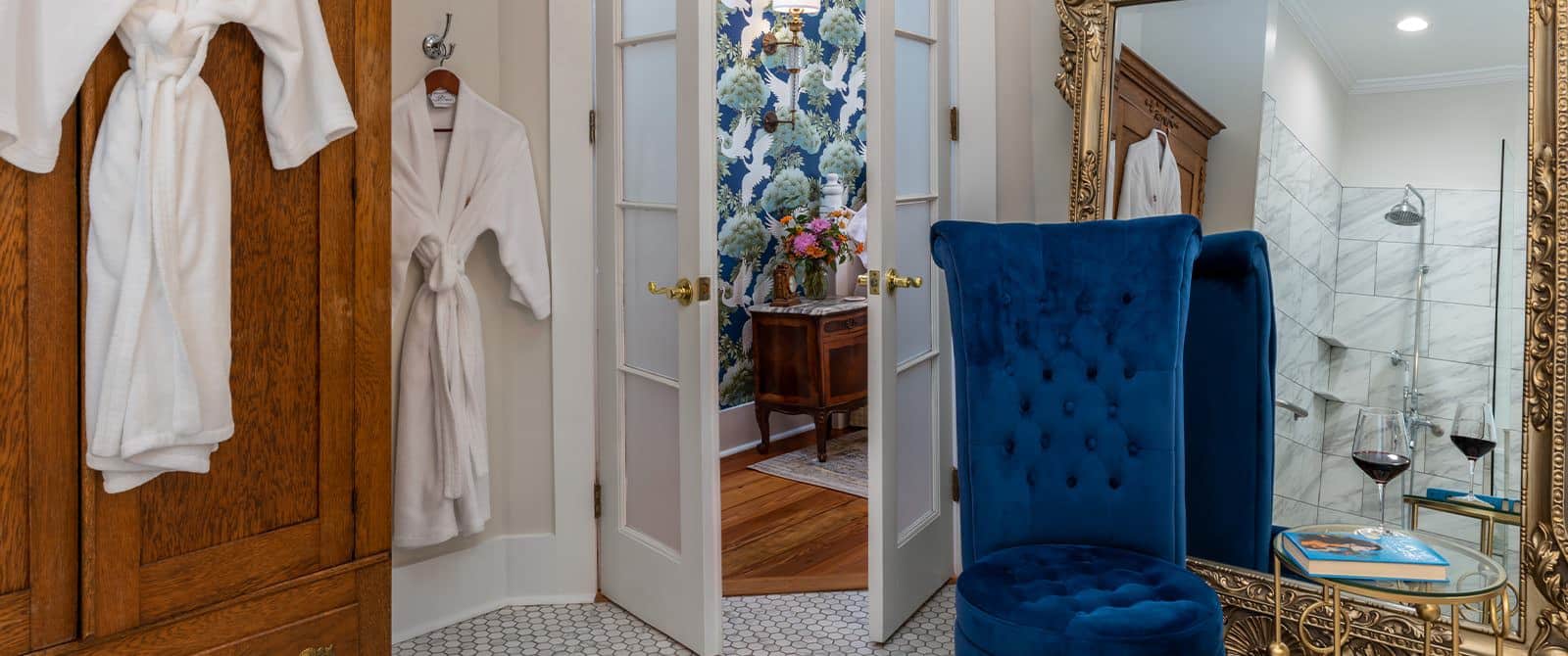 Bathroom with white walls, tiled flooring, wooden dresser, blue upholstered chair, and small table