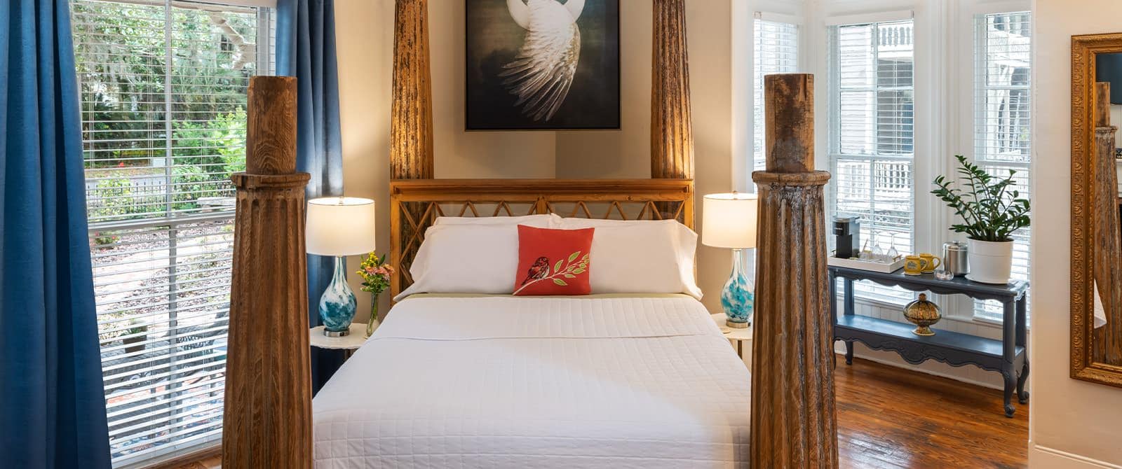 Bedroom with cream walls, hardwood flooring, bed with large wooden posts, white bedding, and large windows