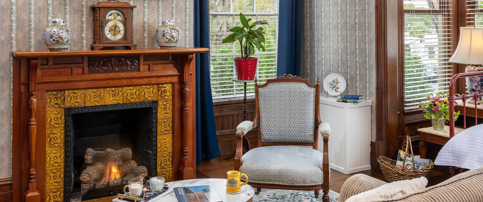 Bedroom with ornate wallpaper, hardwood flooring, sitting area, and fireplace with wooden mantel