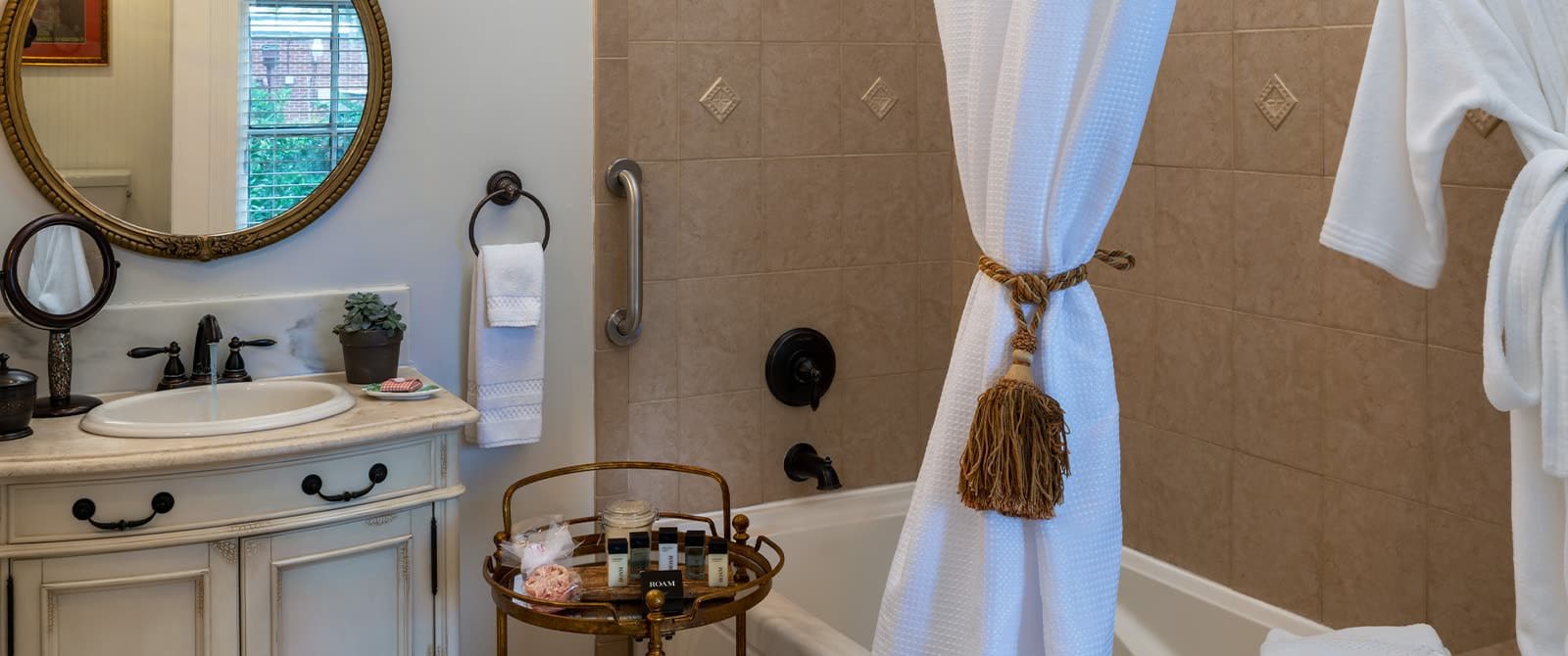 Bathroom with white walls, tiled tub and shower combination, framed circle mirror, and white vanity