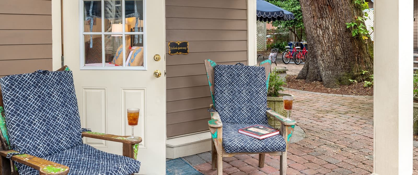 Stone patio with wooden chairs with navy and white cushions and large tree in the background