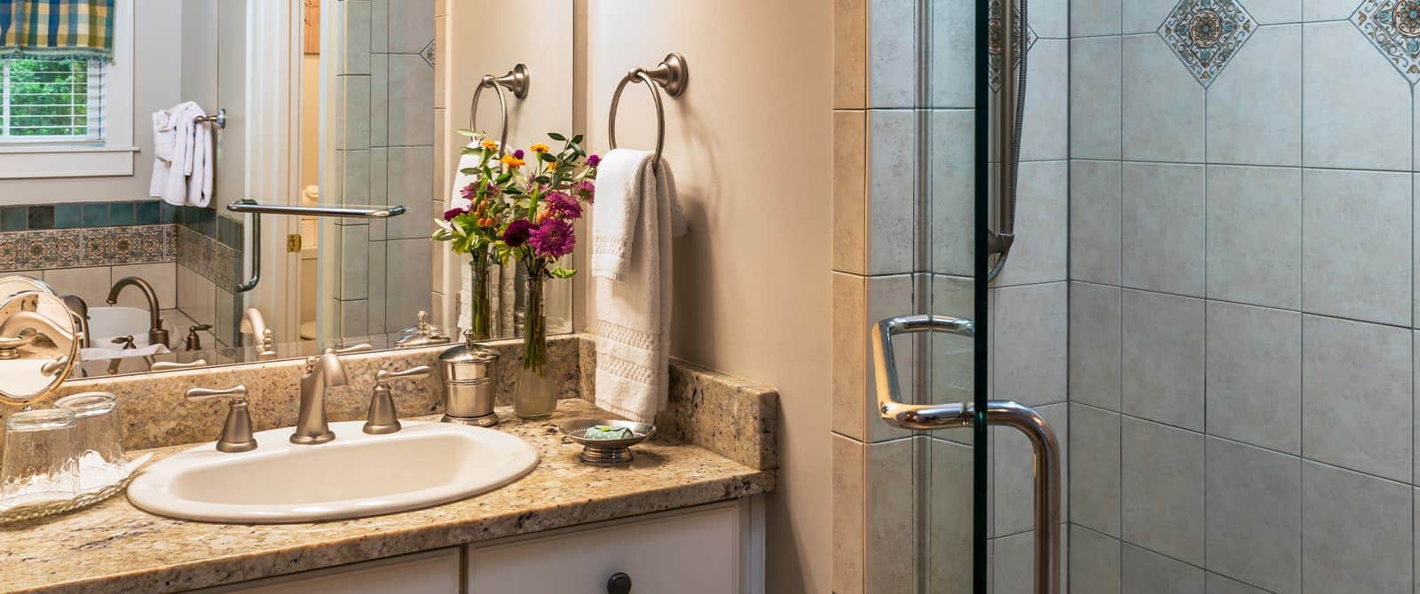 Bathroom with light colored walls, tiled walk in shower, white vanity with quartz top, and large mirror