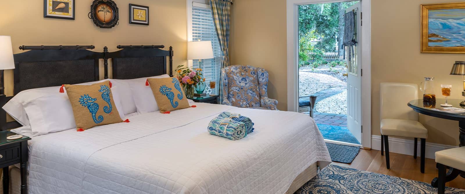 Bedroom with cream walls, hardwood flooring, custom headboard, white bedding, upholstered chair, and sitting area