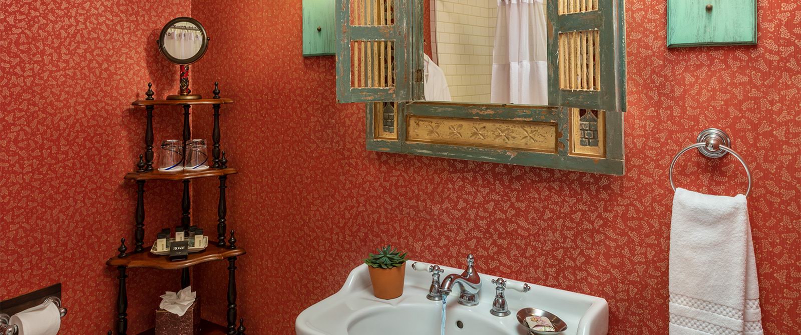 Bathroom with wallpaper, white sink, wooden mirror, and wooden corner shelving unit