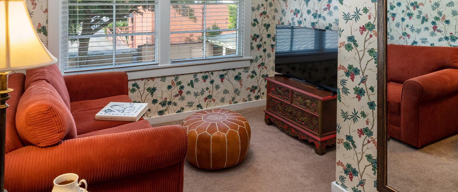 Bedroom's sitting area with upholstered loveseat, ornate dresser, and flat-screen TV