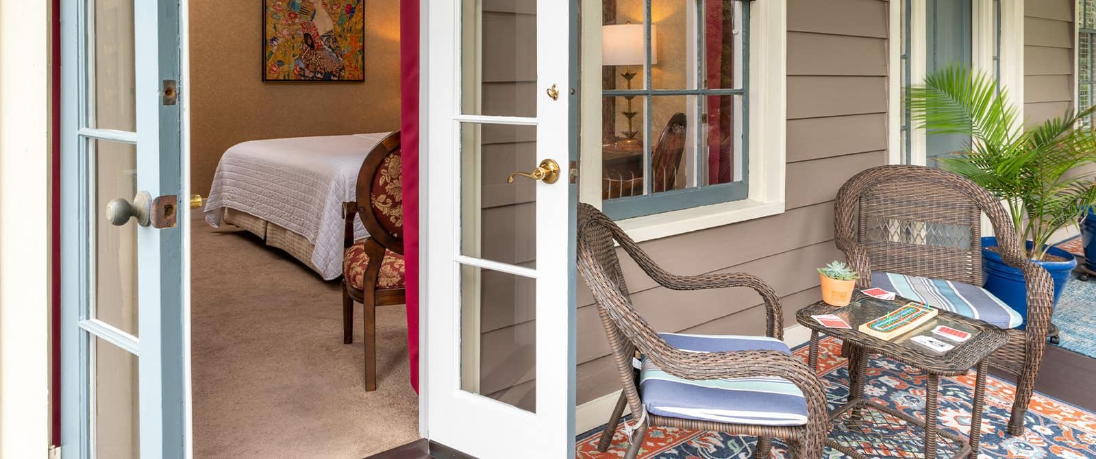 Balcony with wicker patio chairs and table, area rug, potted plant, and view into bedroom