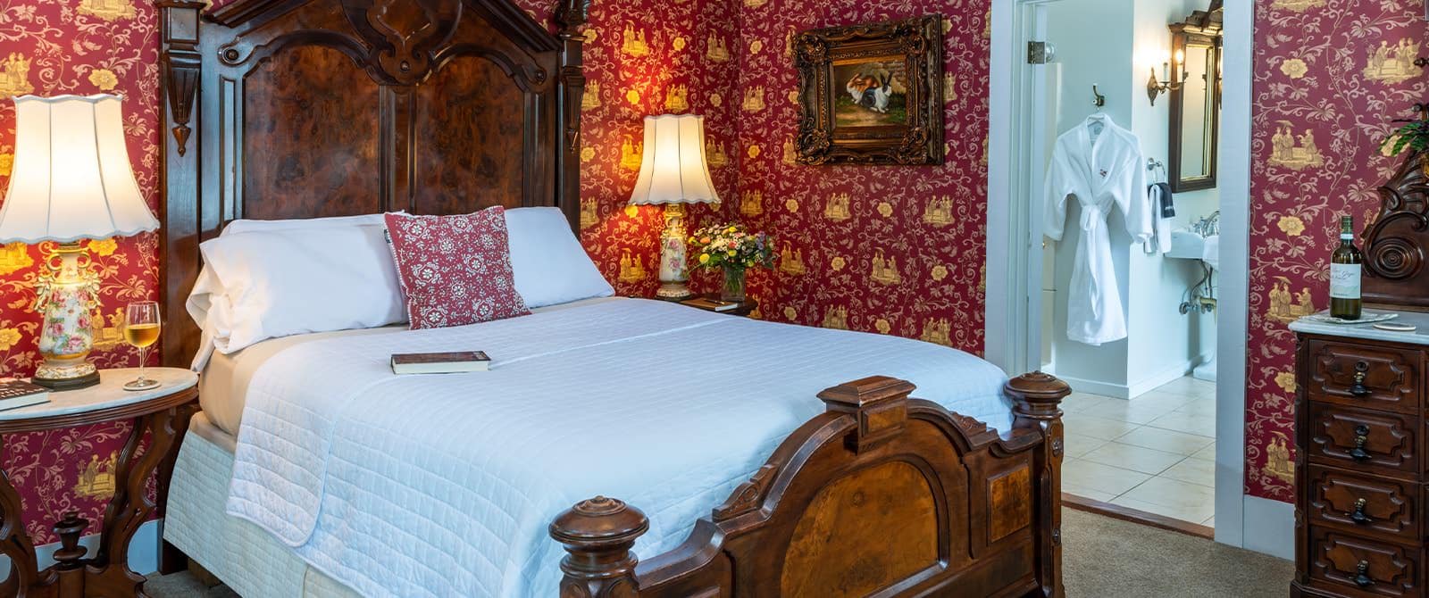 Bedroom with red ornate wallpaper, carpeting, wooden bed, white bedding, and wooden dresser