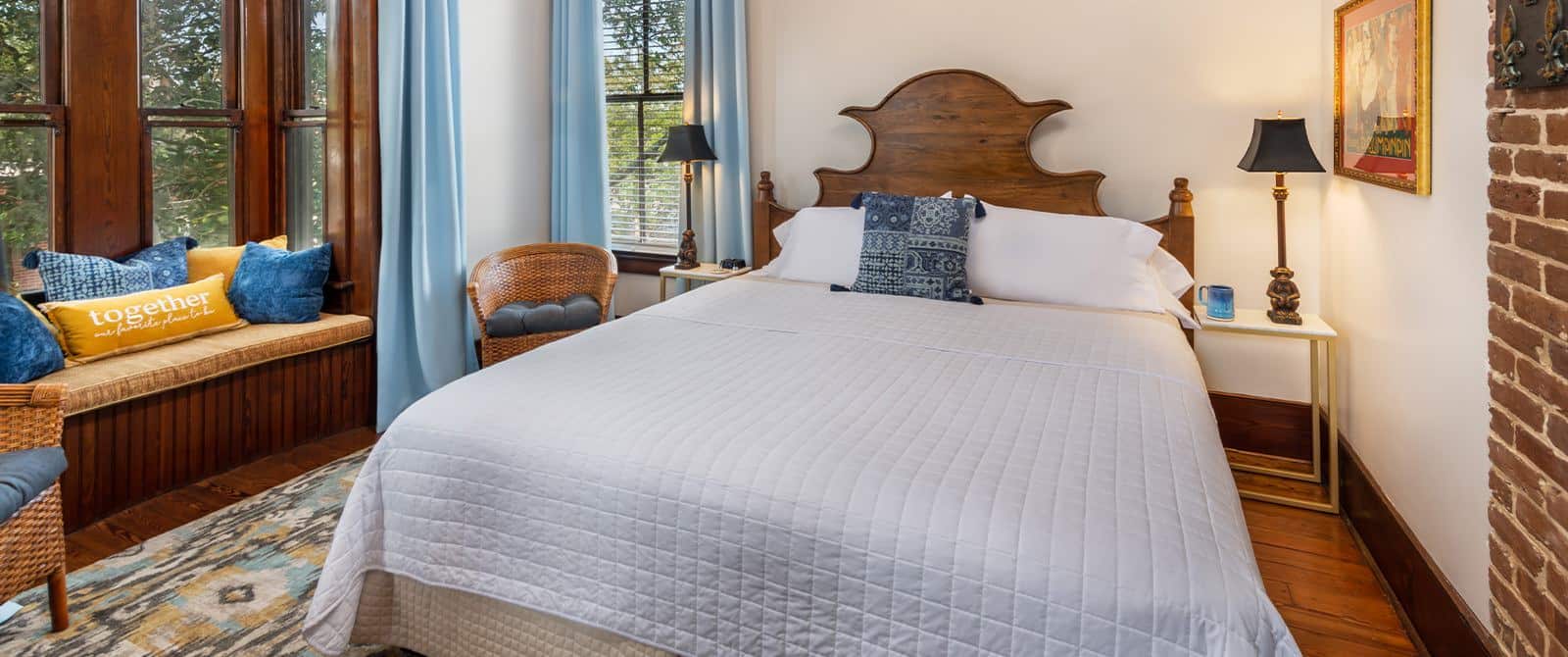 Bedroom with white walls, wooden flooring, wooden headboard, white bedding, and large nook with orange and blue pillows