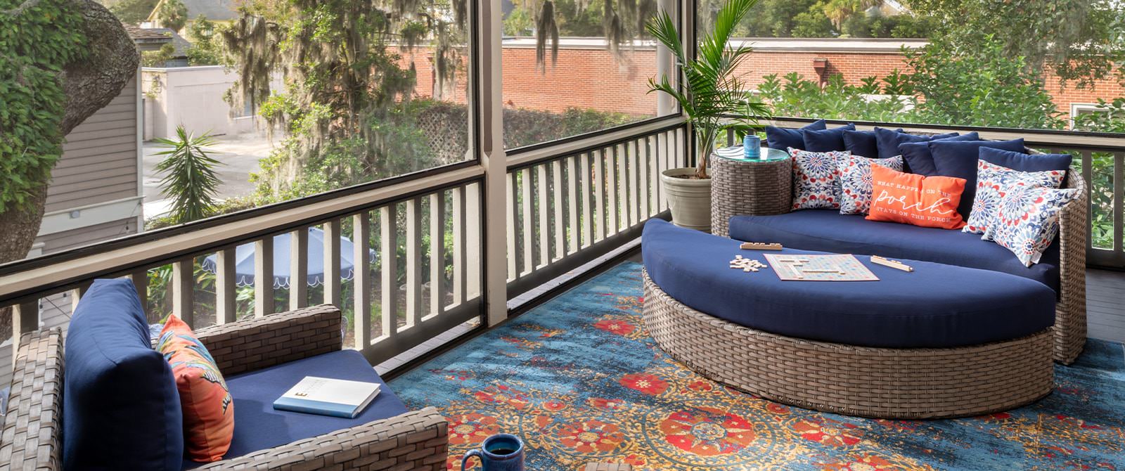 Large screened in porch on second level with light wicker patio furniture with blue fabric and large area rug