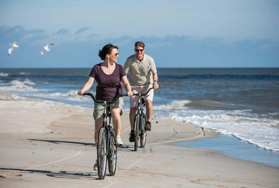 Two people riding bikes on the beach