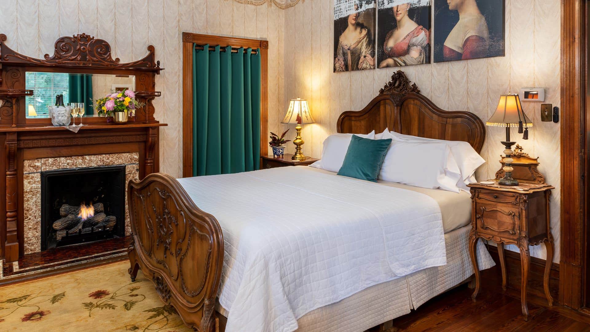 Bedroom with wallpaper, hardwood flooring, wooden bed, white bedding, and fireplace with wooden mantel and mirror