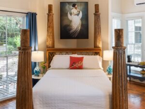 Bedroom with cream walls, hardwood flooring, bed with large wooden posts, white bedding, and large windows