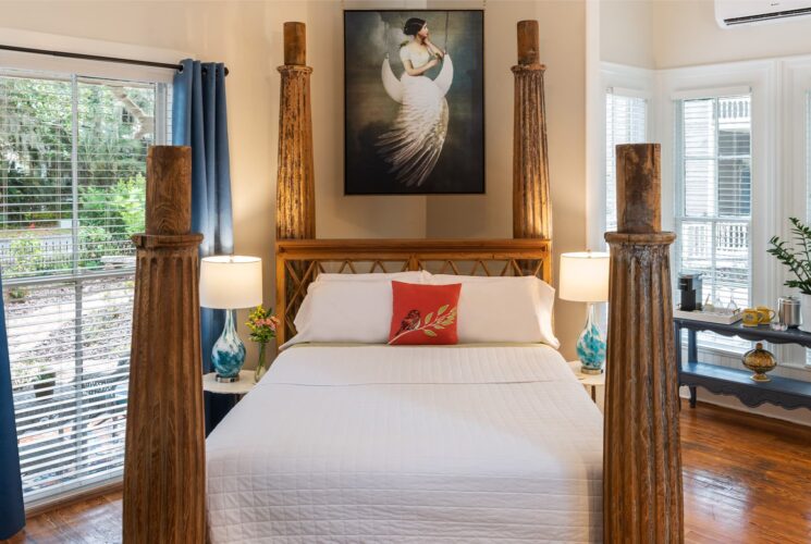 Bedroom with cream walls, hardwood flooring, bed with large wooden posts, white bedding, and large windows