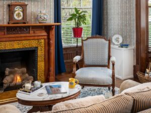 Bedroom with ornate wallpaper, hardwood flooring, sitting area, and fireplace with wooden mantel