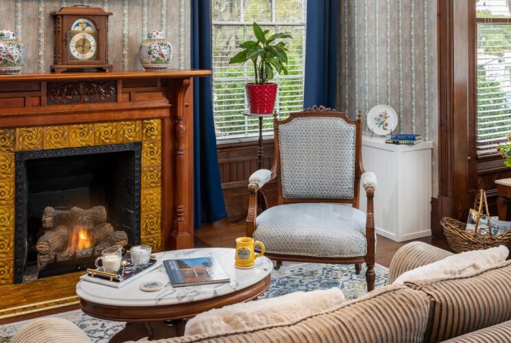 Bedroom with ornate wallpaper, hardwood flooring, sitting area, and fireplace with wooden mantel