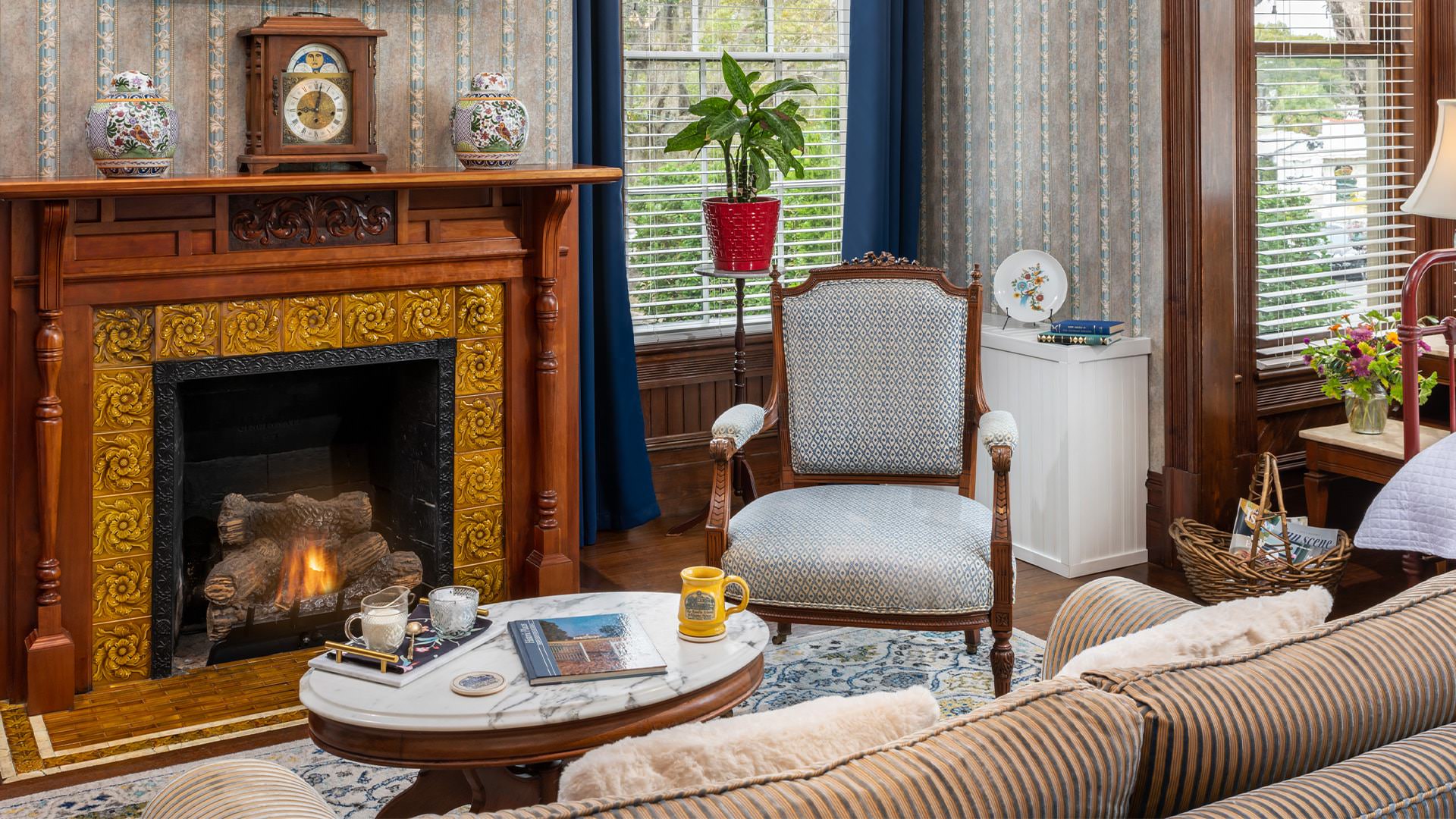 Bedroom with ornate wallpaper, hardwood flooring, sitting area, and fireplace with wooden mantel