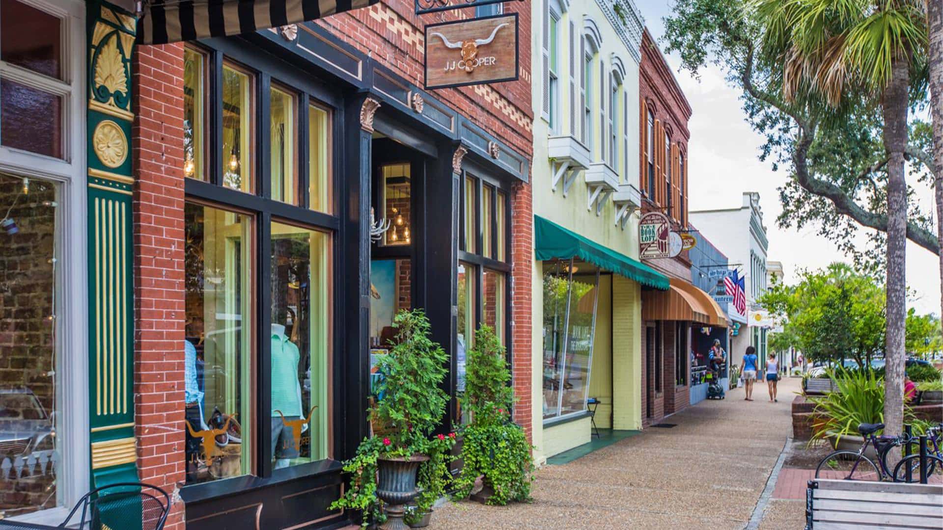 Retail store fronts in a small downtown area surrounded by green trees