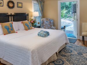 Bedroom with cream walls, hardwood flooring, custom headboard, white bedding, upholstered chair, and sitting area