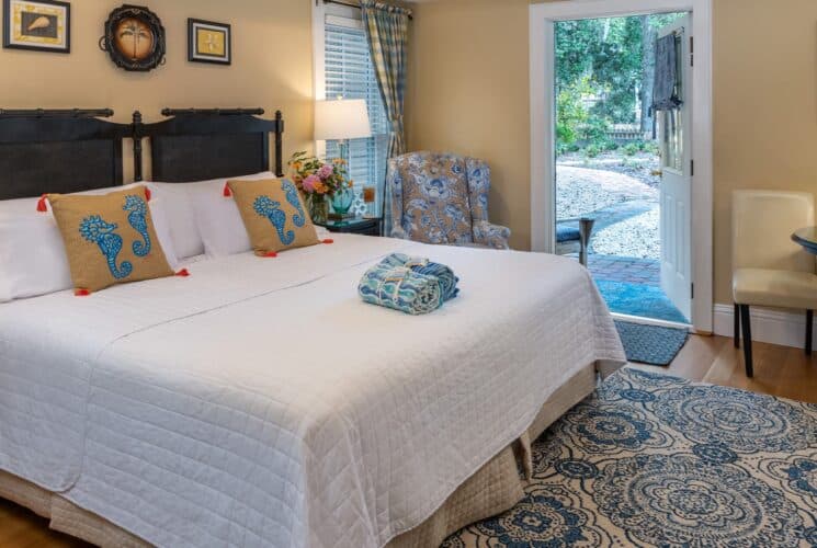 Bedroom with cream walls, hardwood flooring, custom headboard, white bedding, upholstered chair, and sitting area