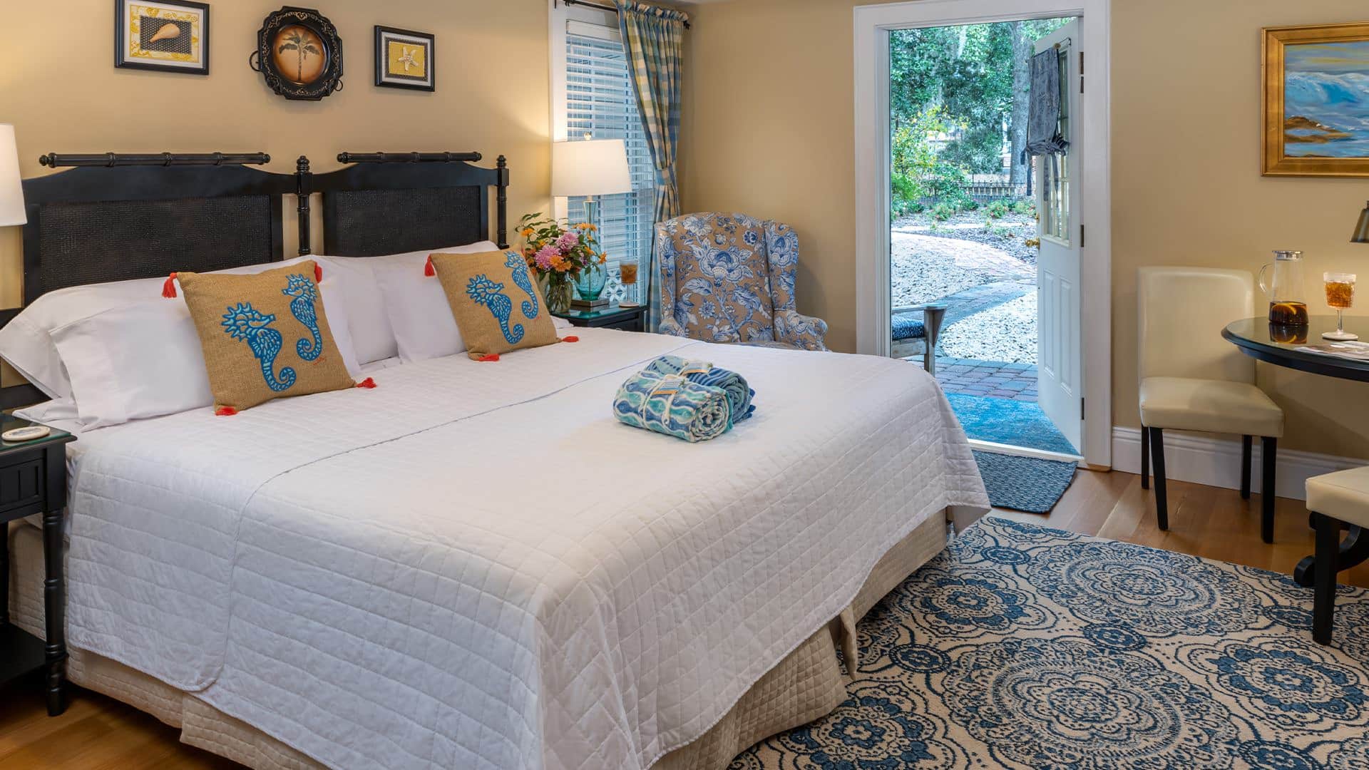 Bedroom with cream walls, hardwood flooring, custom headboard, white bedding, upholstered chair, and sitting area