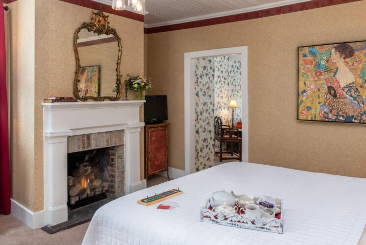 Bedroom with wallpaper, white bedding, fireplace with white mantel, and ornate mirror