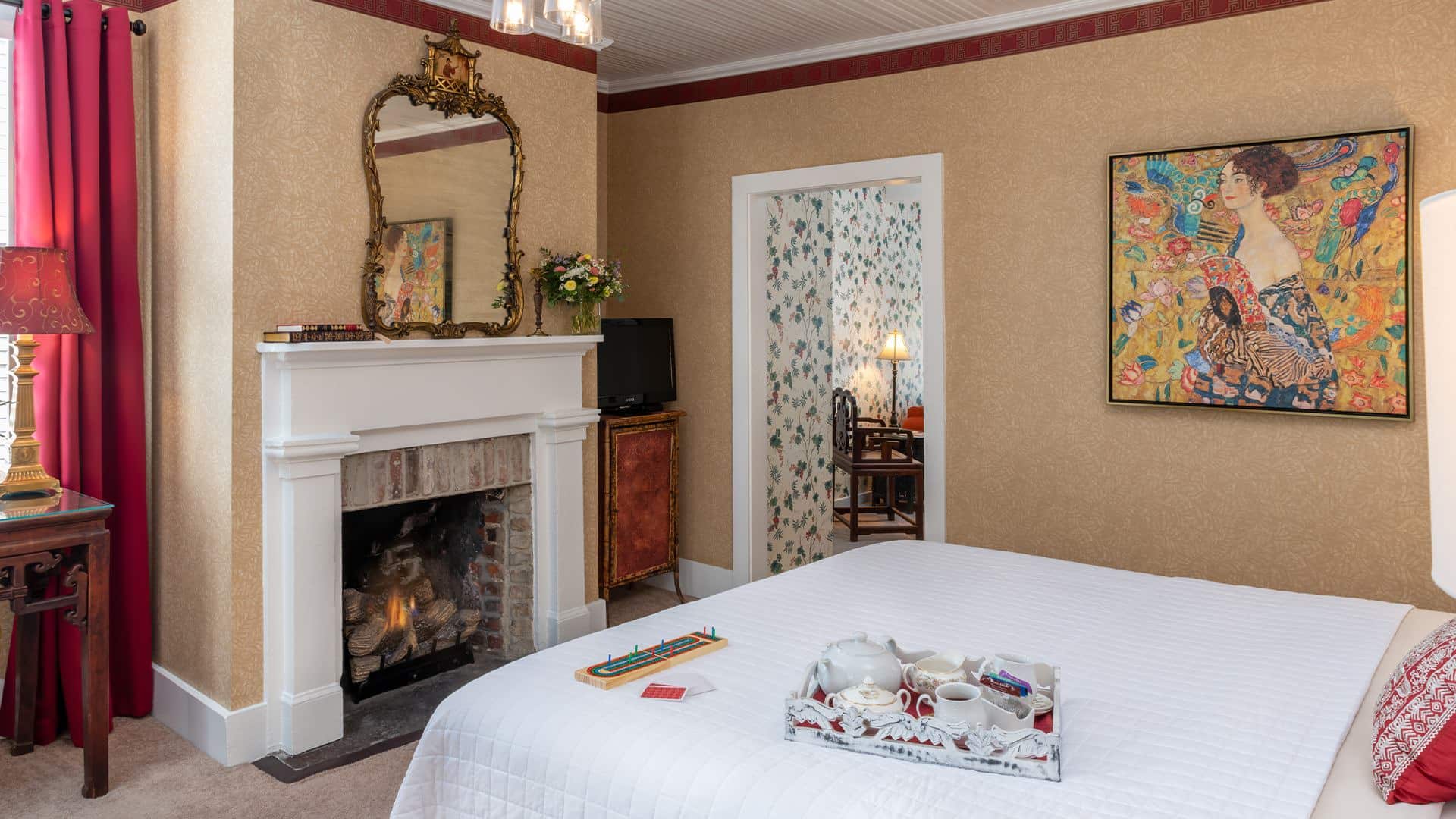 Bedroom with wallpaper, white bedding, fireplace with white mantel, and ornate mirror