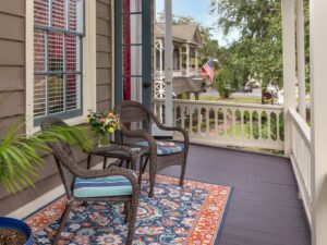 Balcony with dark wicker patio chairs and table, area rug, and potted plant