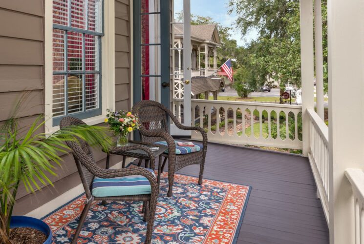 Balcony with dark wicker patio chairs and table, area rug, and potted plant