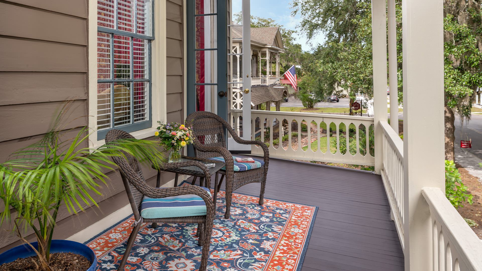 Balcony with dark wicker patio chairs and table, area rug, and potted plant