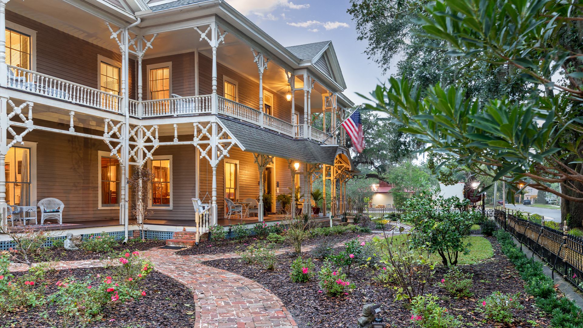 Exterior view of the property painted pale plum with white trim surrounded by green trees, bushes, and many flowers