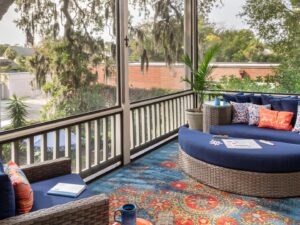 Large screened in porch on second level with light wicker patio furniture with blue fabric and large area rug