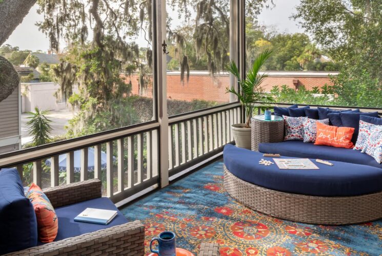 Large screened in porch on second level with light wicker patio furniture with blue fabric and large area rug