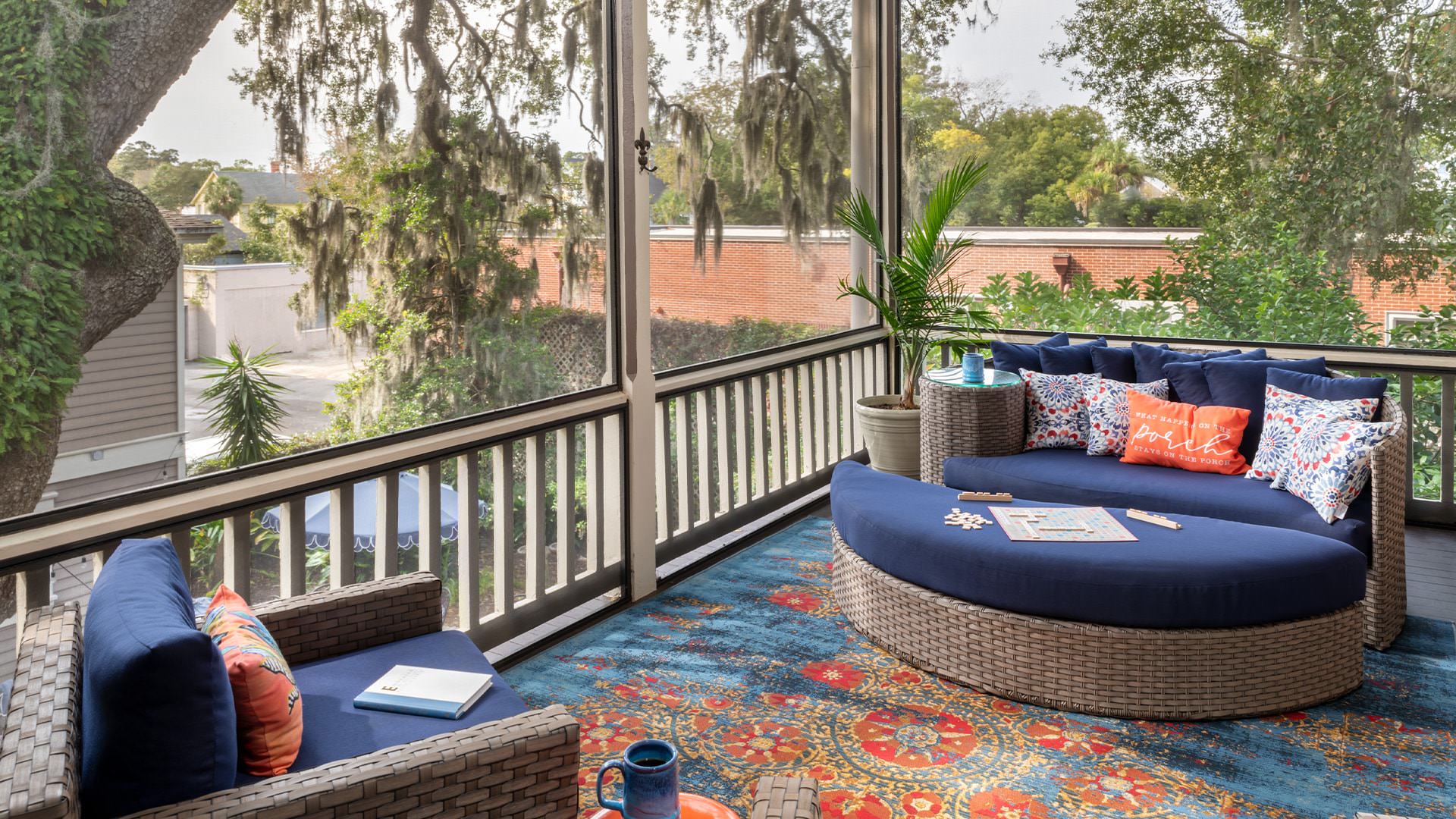 Large screened in porch on second level with light wicker patio furniture with blue fabric and large area rug