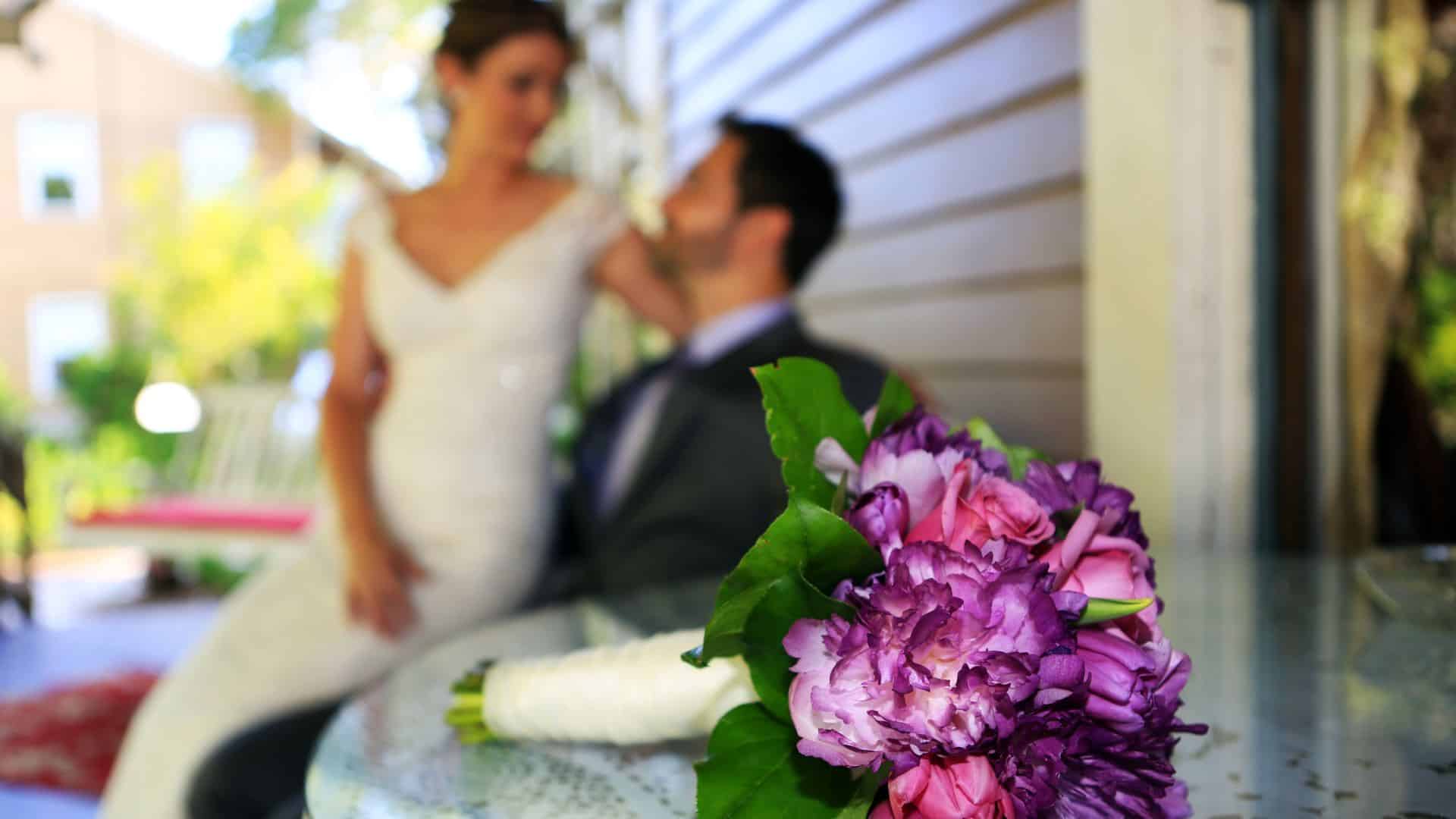 Close up view of bridal bouquet with pink and purple flowers with bride and groom in the background