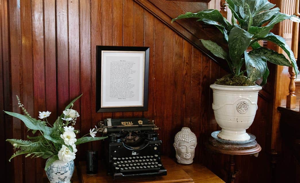 Close up view of antique typewriter, statue head, and large potted vases with dark wooden staircase paneling behind them