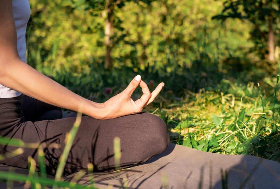 Close up view of a person sitting on a mat on green grass holding a yoga pose