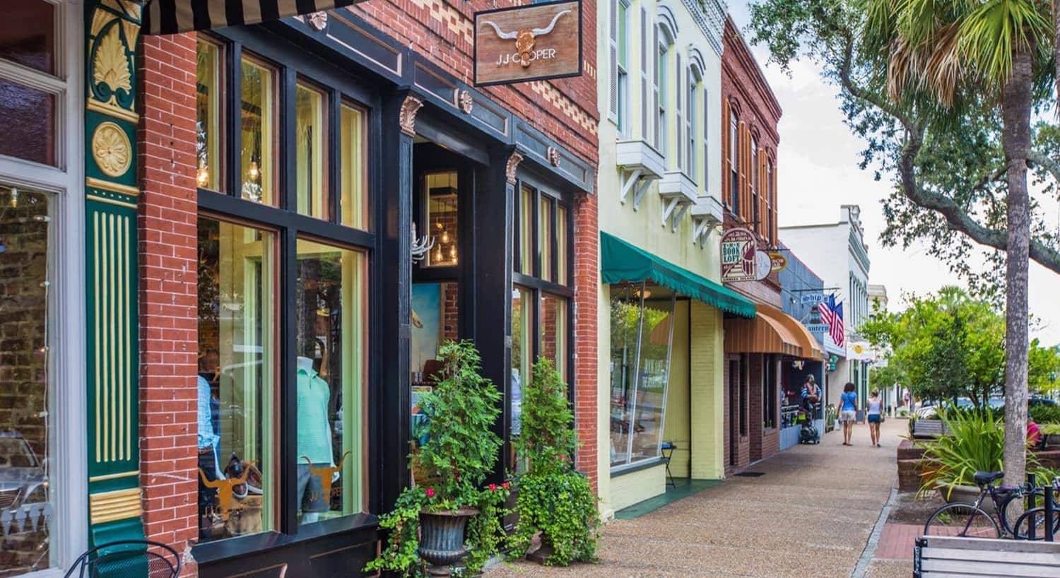 Retail store fronts in a small downtown area surrounded by green trees