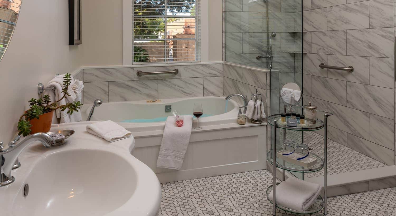 Bathroom with white walls, light gray and white tiling, two person tub, walk-in shower, and white sink