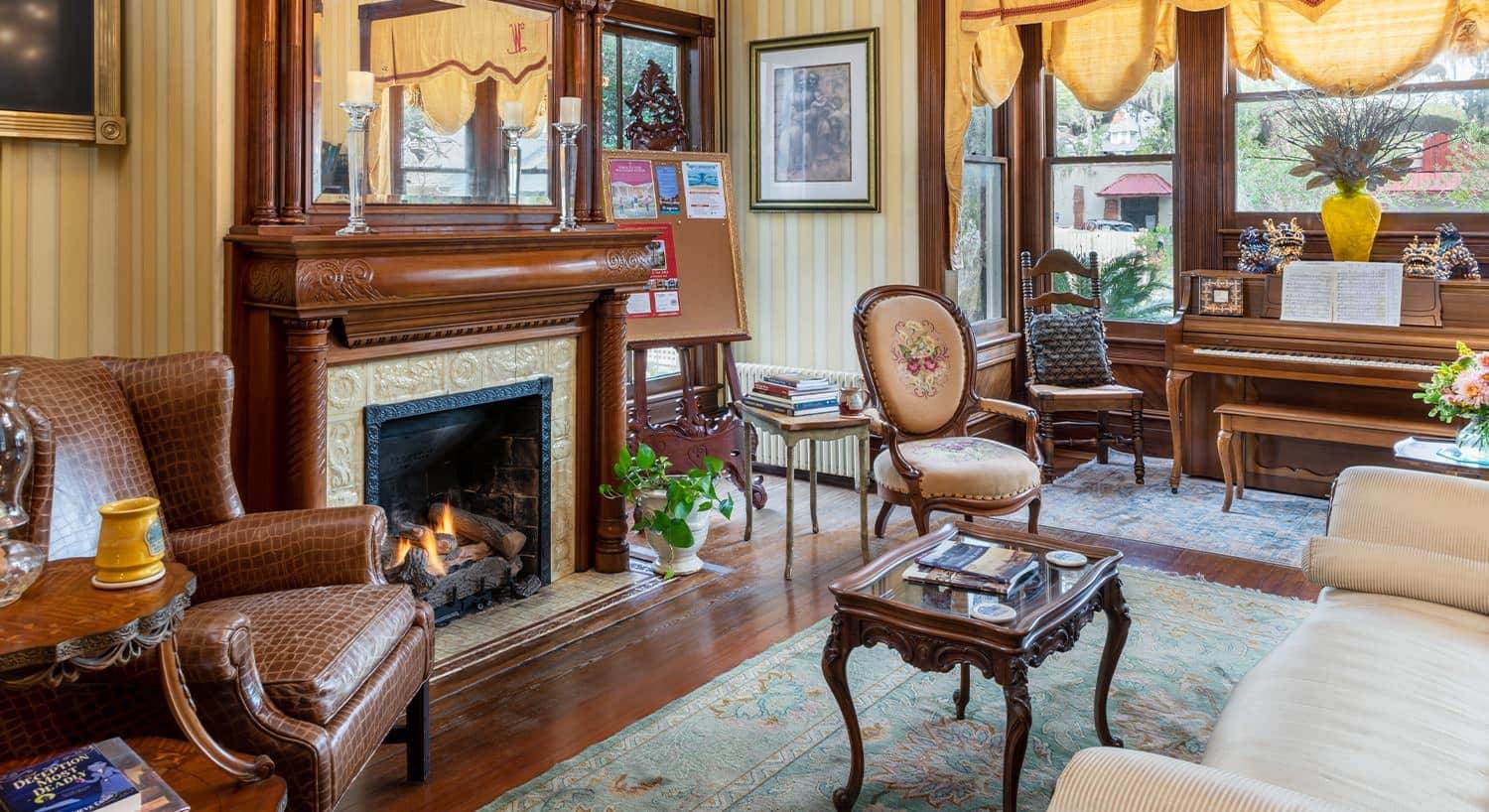 Large room with pale yellow striped wallpaper, hardwood flooring, wooden fireplace, upholstered sofa, and small piano