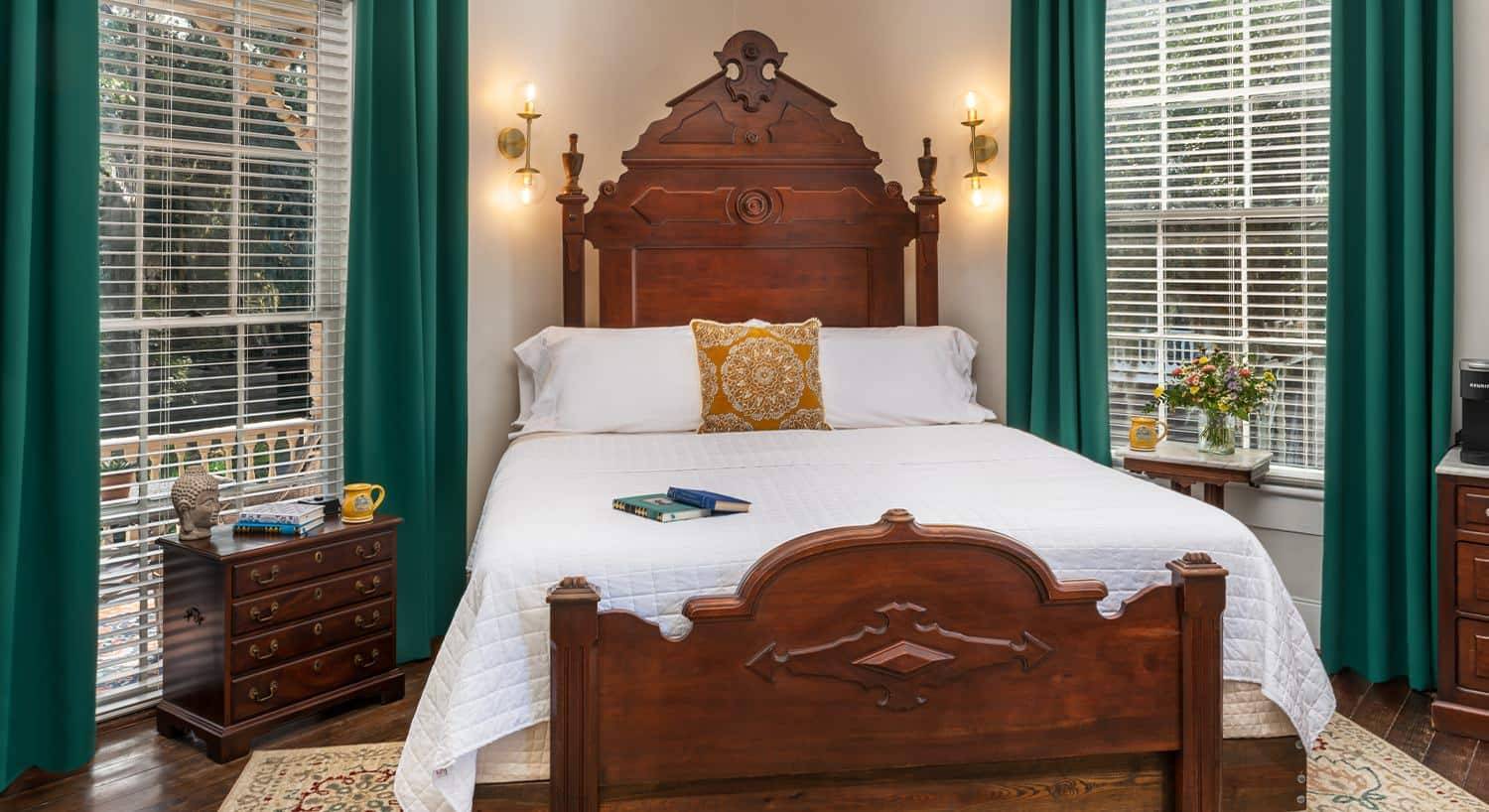 Bedroom with light colored walls, hardwood flooring, dark wooden bed and dressers, white bedding, and two large windows