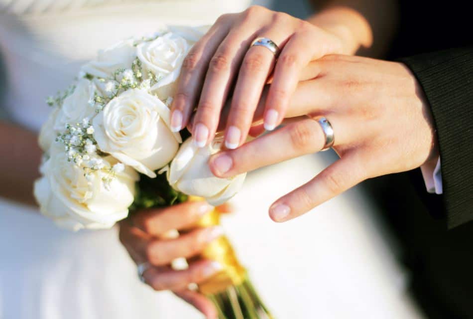Close up view of bridal bouquet of white roses and bride and groom hands with wedding bands
